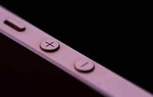 Close-up of volume buttons (+ and -) on a pink electronic device with a dark background.