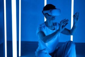 Person in VR headset with hands raised, illuminated by cooler blue lights and vertical light bars.