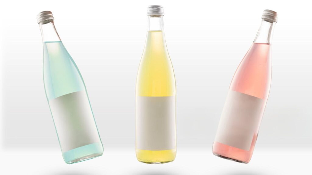 Three glass bottles filled with colored liquids: blue, yellow, and pink, standing against a light background.