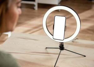 Ring light with a smartphone attached with a tripod in the center on a wooden table.