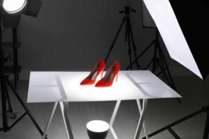 A pair of red high heels on a white table in a photo studio setup with lights and a softbox.