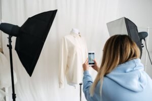 Person photographing a mannequin with a shirt using a smartphone in a studio setup.