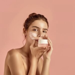 a woman with a face mask on holding a container of cream in a peach color background.