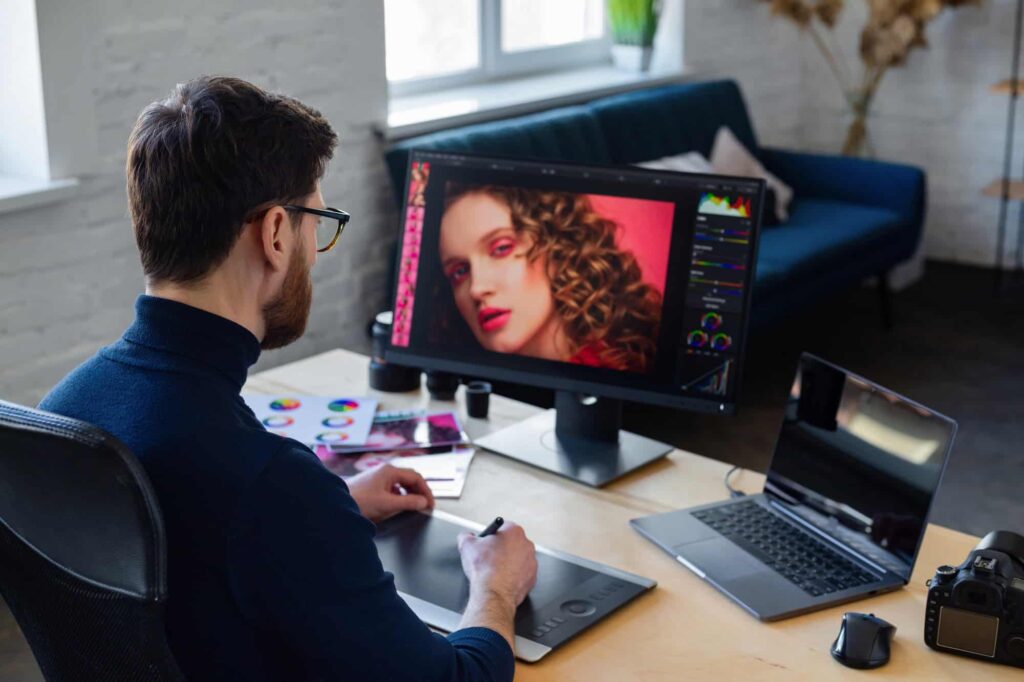 Photo editor using Photoshop tricks to enhance images on a monitor in a modern workspace with photography tools.