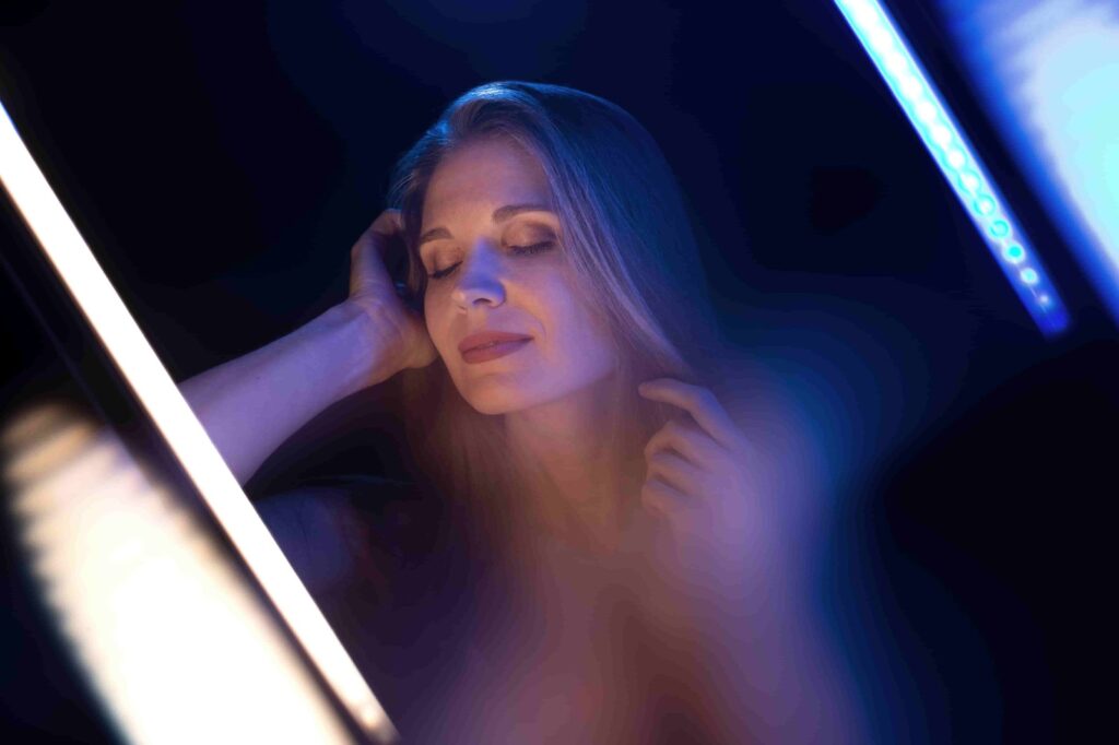 Woman with closed eyes touching face under blue and white lighting, illustrating the impact of lighting mistakes in photo editing.