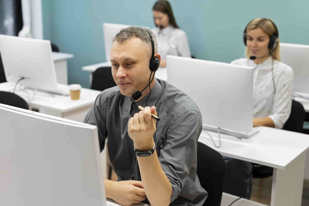 Customer support team member assisting clients at clipping path company office with colleagues collaborating in background.