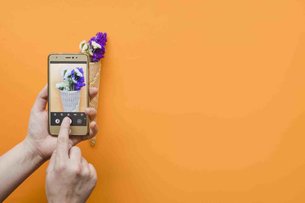 Beginner capturing floral photo with smartphone for mobile editing practice on a vibrant orange background.