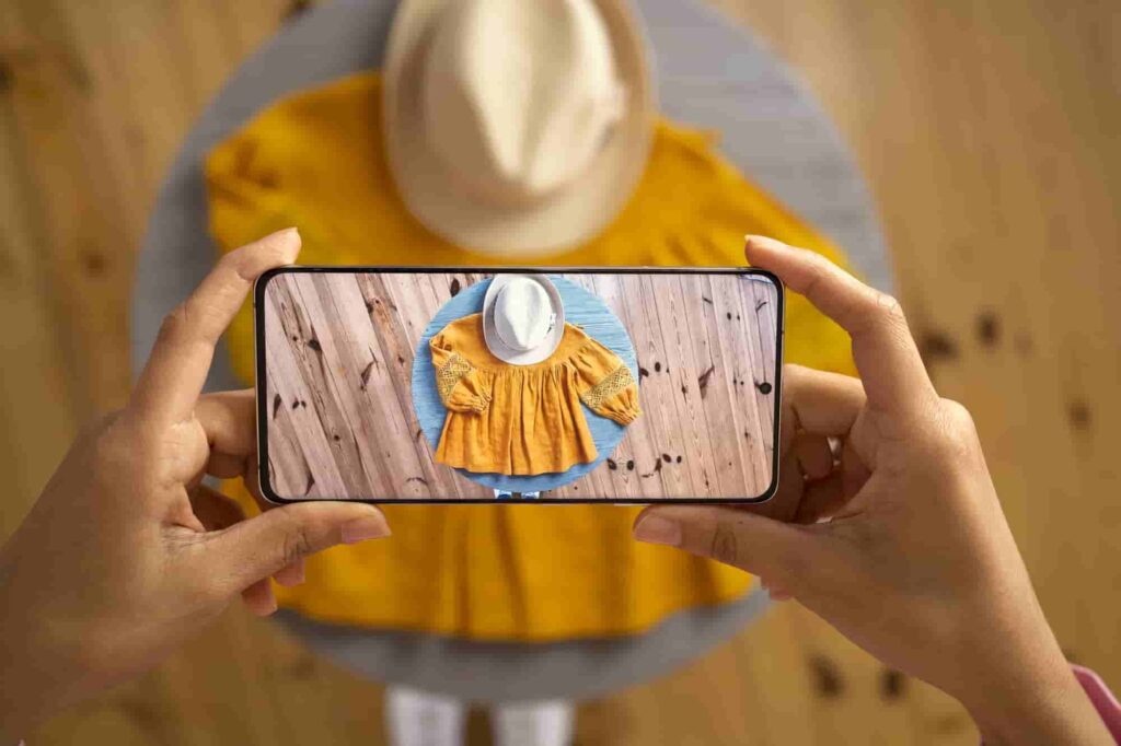 Beginner taking a flat lay photo with smartphone of fashion items for mobile editing practice on a wooden surface.