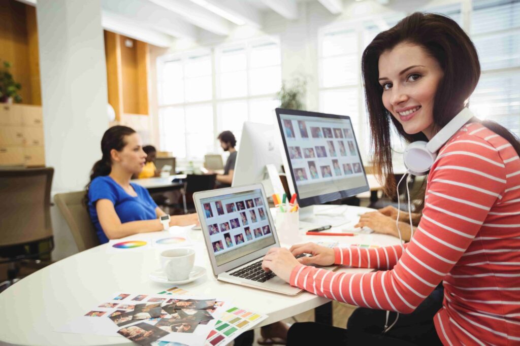 Fashion designer working on ghost mannequin editing and product images at a modern office with design materials and laptop.