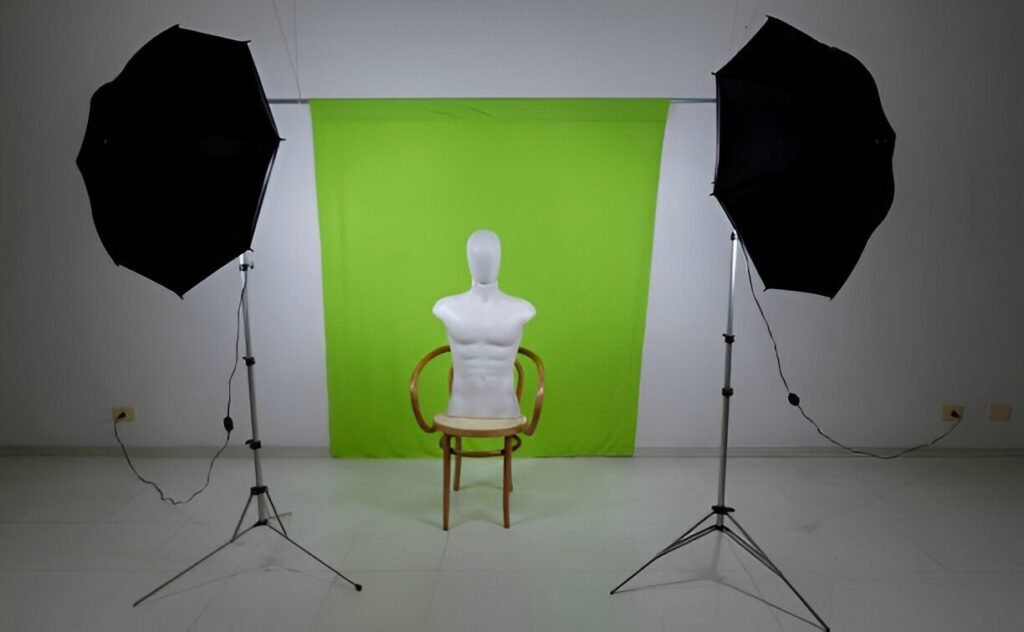 A white mannequin sits on a chair in front of a vibrant green backdrop, flanked by two black umbrella studio lights.