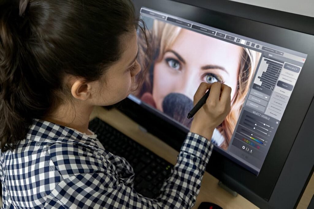 A person with long hair, wearing a checkered shirt, works on a computer with a large touchscreen, editing digital images.