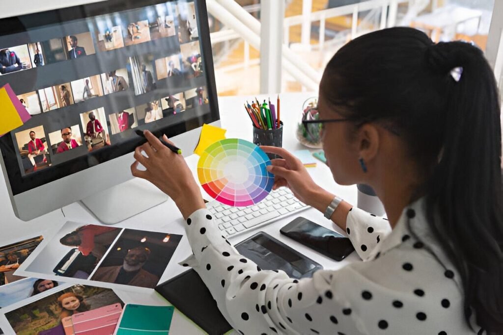 A person in a polka dot shirt works at a desk with color palettes, photos, and a computer displaying various images.