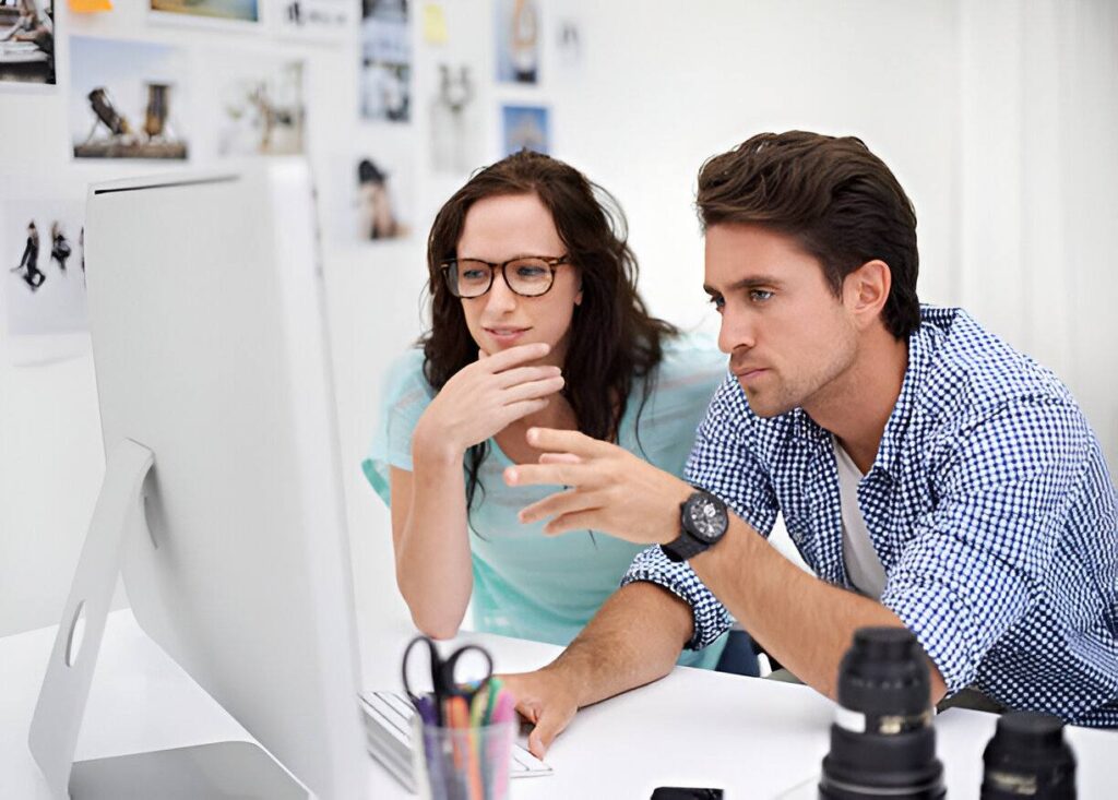 Two individuals collaborate at a desk, discussing design ideas while surrounded by photography equipment and inspiration boards.