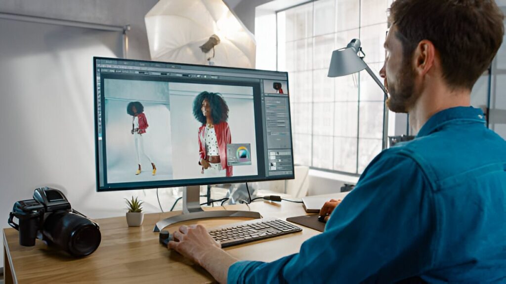 A person editing fashion images on a large monitor in a well-lit studio, with a camera and workspace visible.