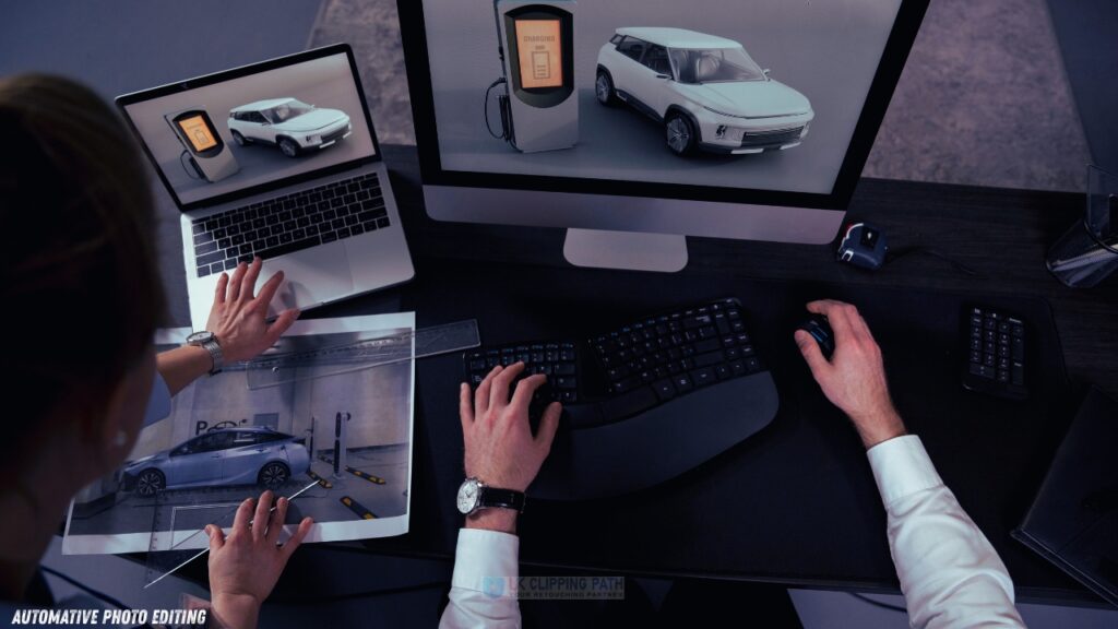 A designer edits automotive images on a laptop and monitor, with printed photos and tools on a desk, showcasing modern car technology.