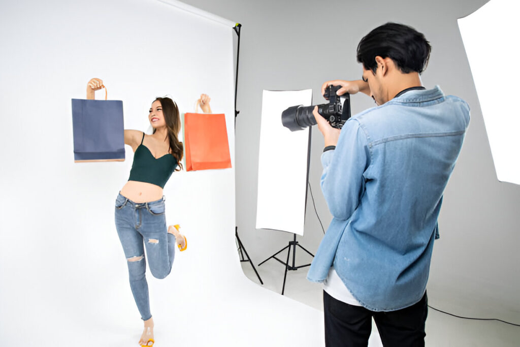 A model poses with colorful shopping bags while a photographer captures the moment in a well-lit studio setting.