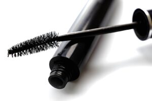 A black mascara tube with a brush partially pulled out, resting on a white surface, showcasing its bristles and glossy finish.