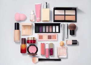 Assorted makeup products arranged neatly on a light background, including palettes, brushes, lipsticks, foundation bottles, and a blending sponge, conveying elegance.