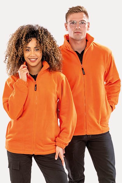 A couple wearing orange jackets, standing side by side, smiling and looking at the camera.